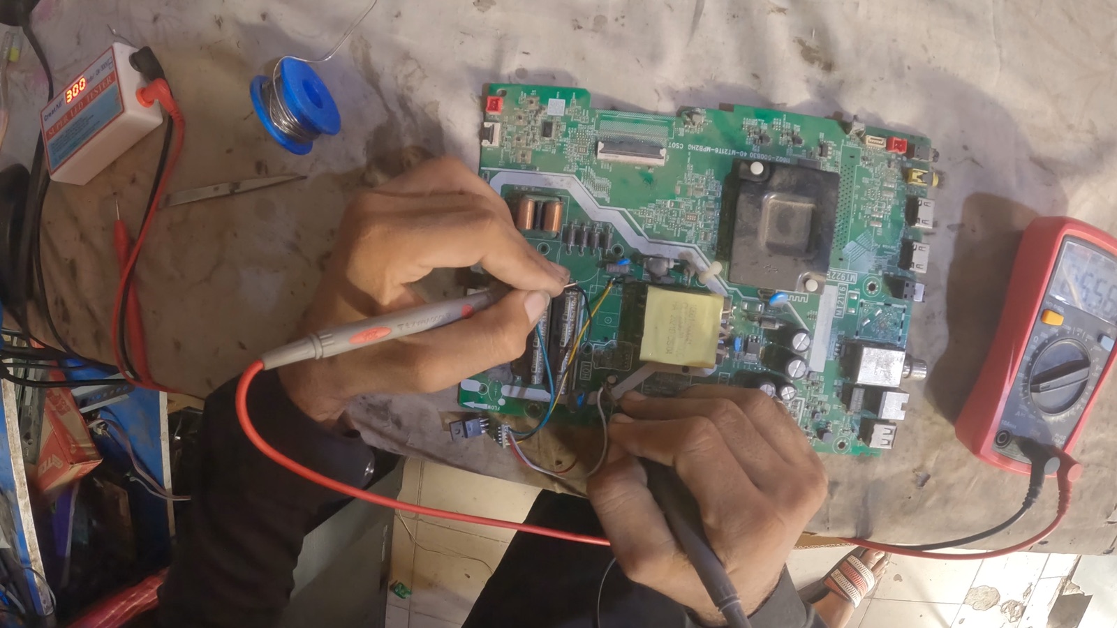 Hands probing components on a television circuit board