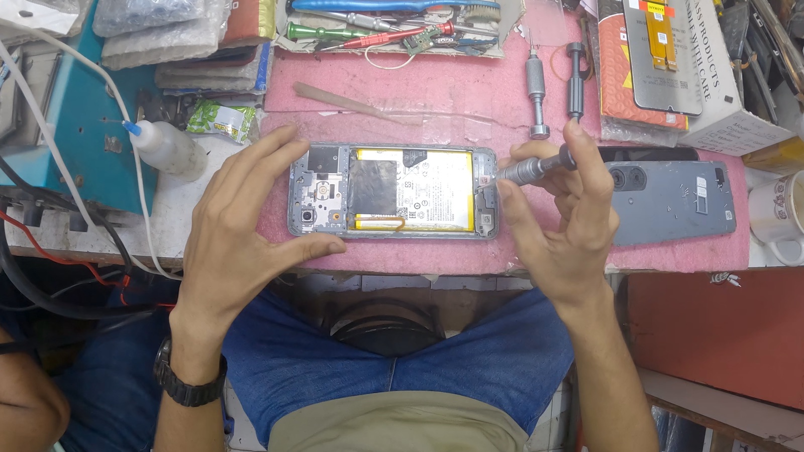 Hands opening a smartphone at an electronics repair bench