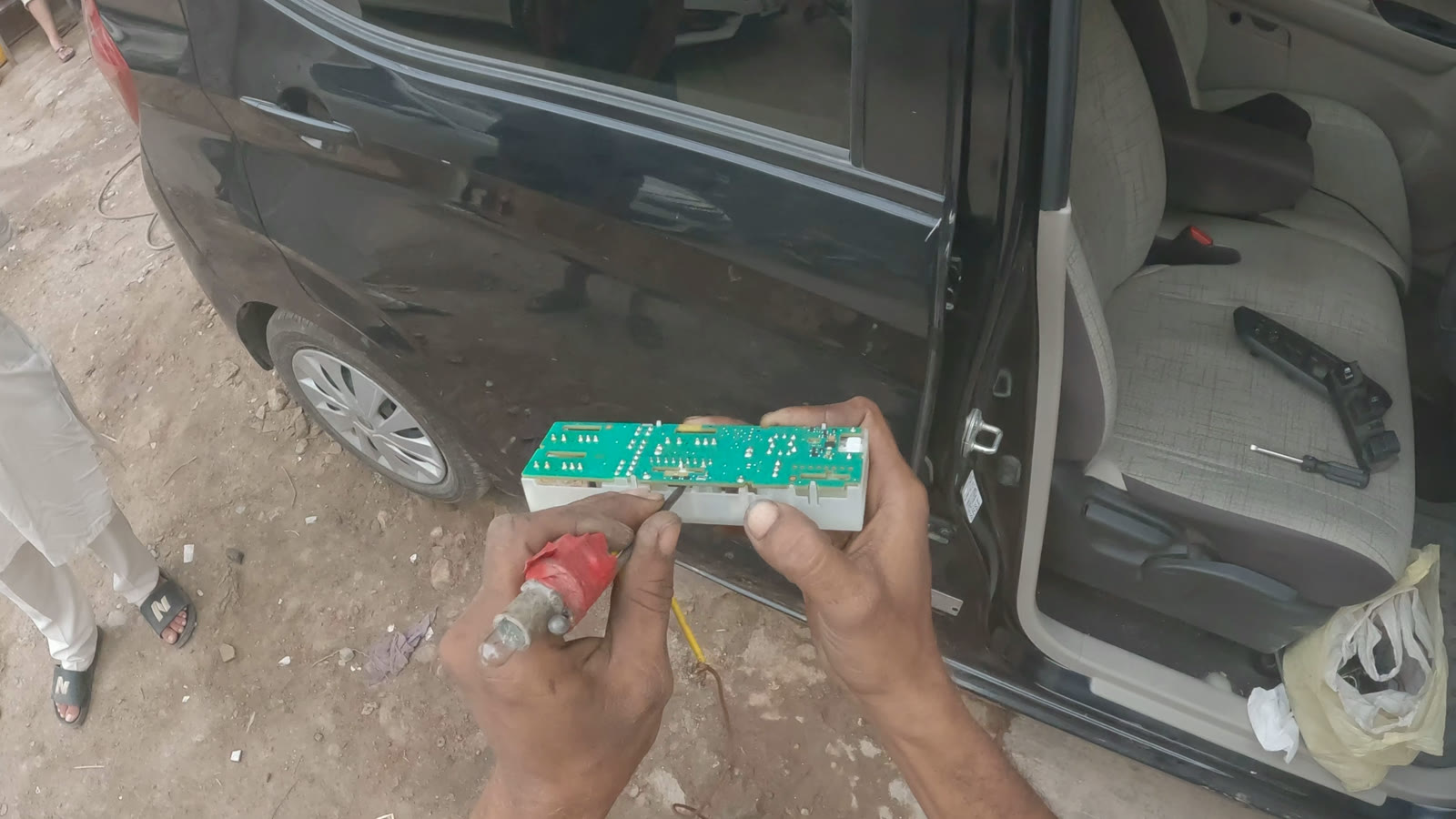 Hands holding a vehicle electrical module beside an open car