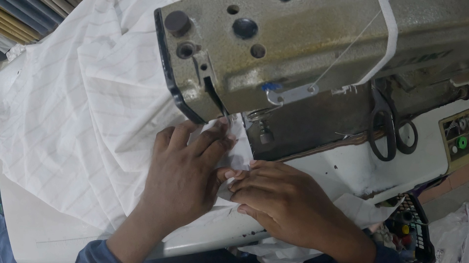 Close first-person view of hands stitching white fabric at a sewing machine